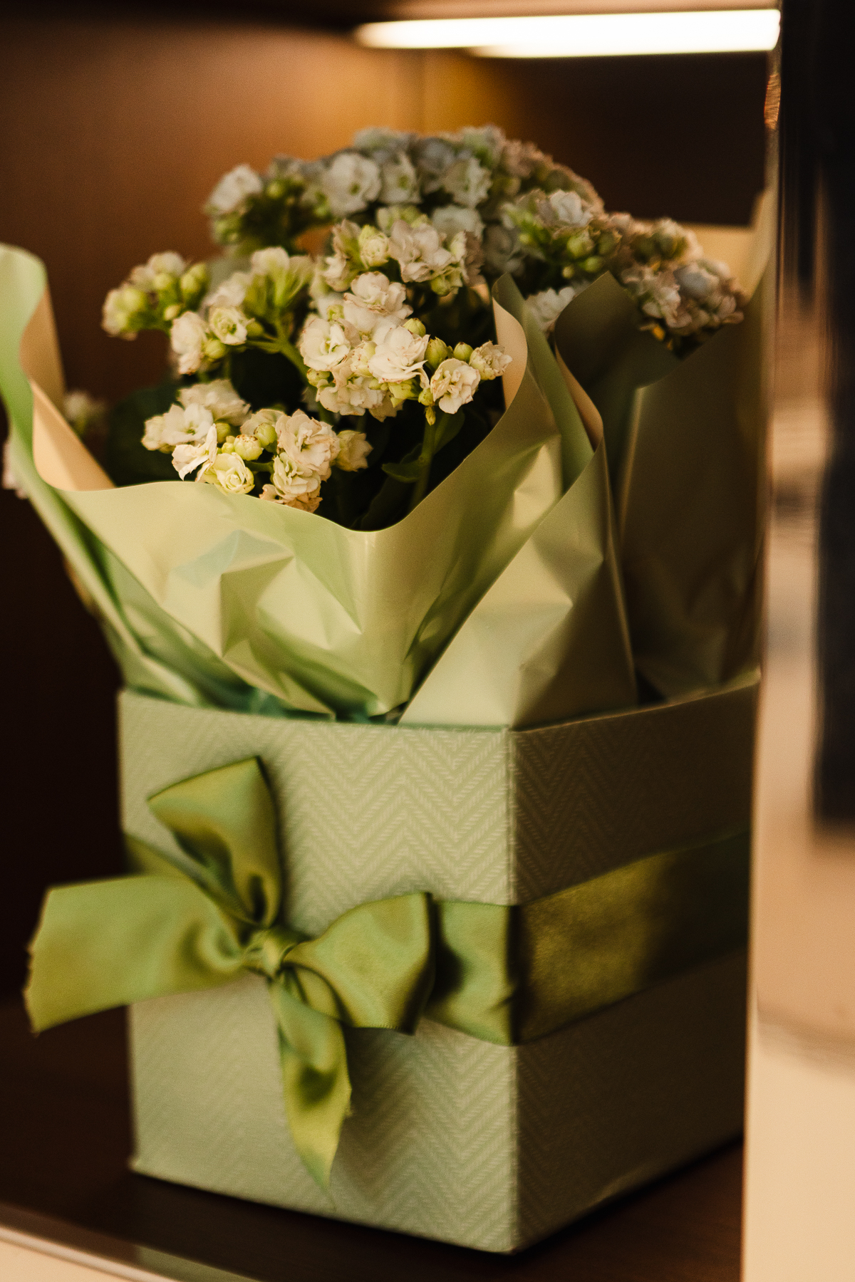 Caixa-presente verde com laço de cetim, contendo flores claras envolvidas em papel de embrulho